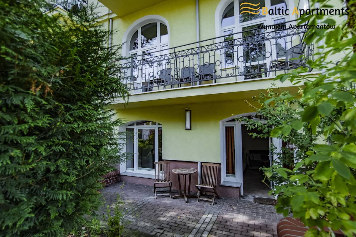 Een gebouw met twee verdiepingen, een balkon, een terras van baksteen en twee houten stoelen.