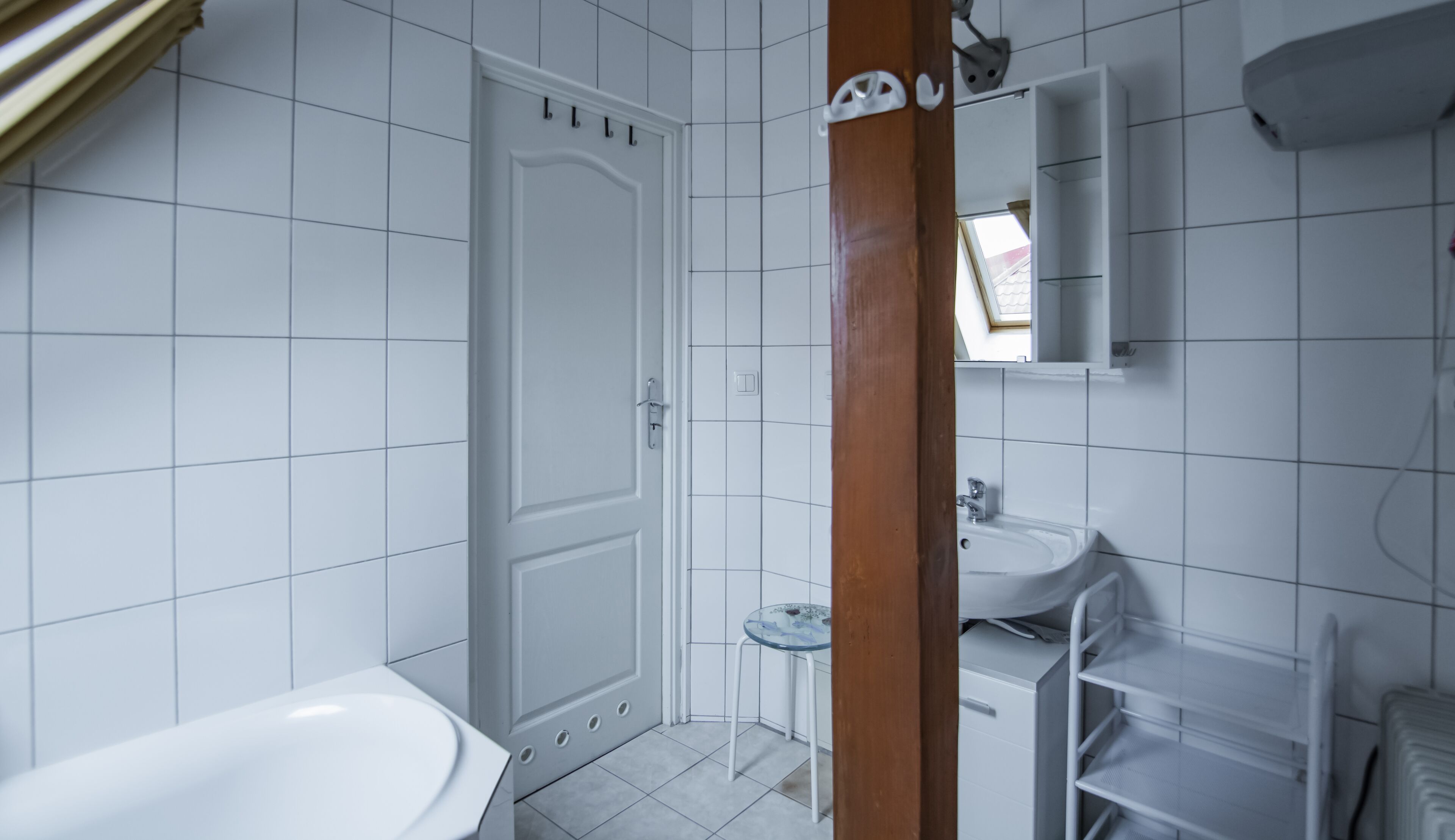 A bathroom with white tiles, a white bathtub, a small glass table, a white sink, and a mirror above the sink.
