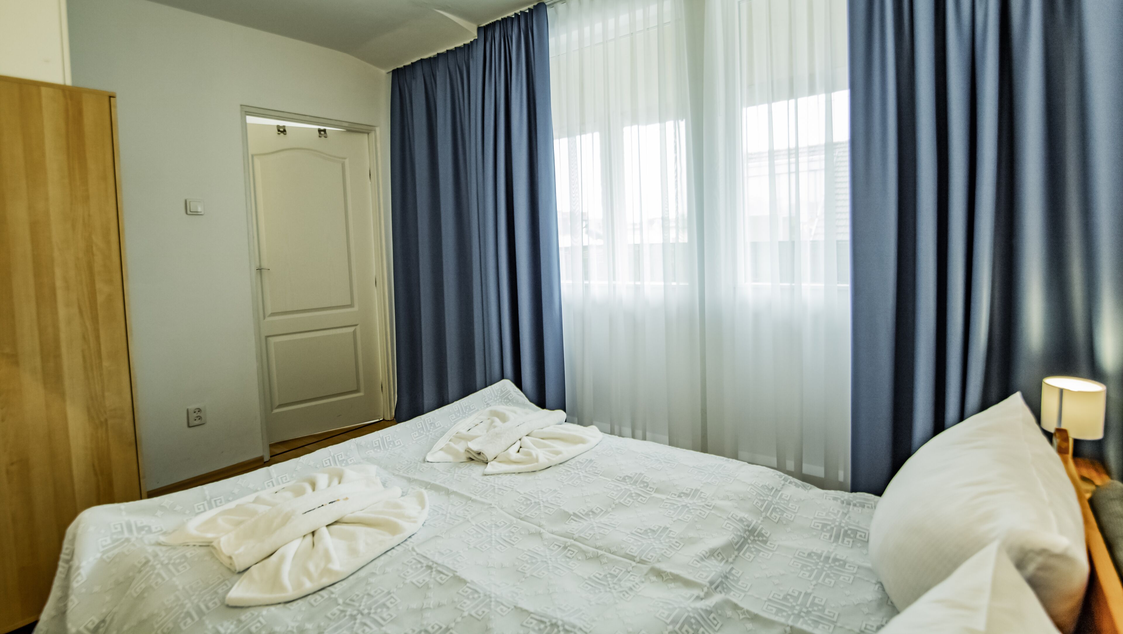 Ein Hotelzimmer mit einem Bett, einem Holzschrank, einer Tür und blauen Vorhängen.