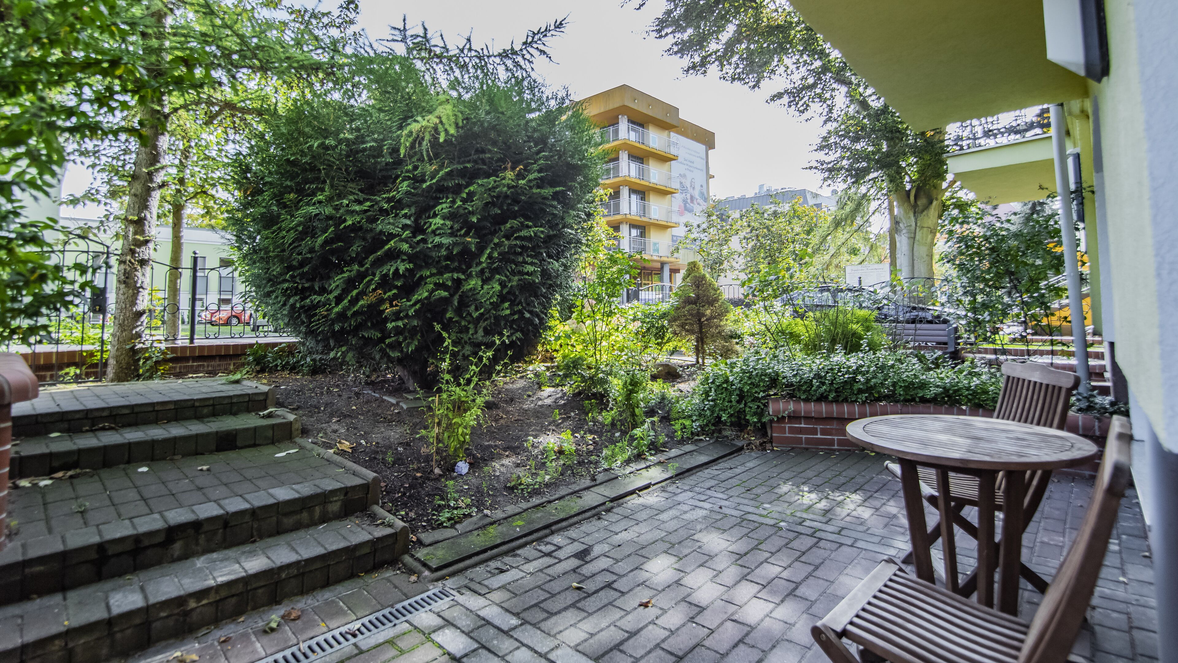 Un patio con sendero de ladrillo, una mesa y sillas de madera, y un árbol grande.