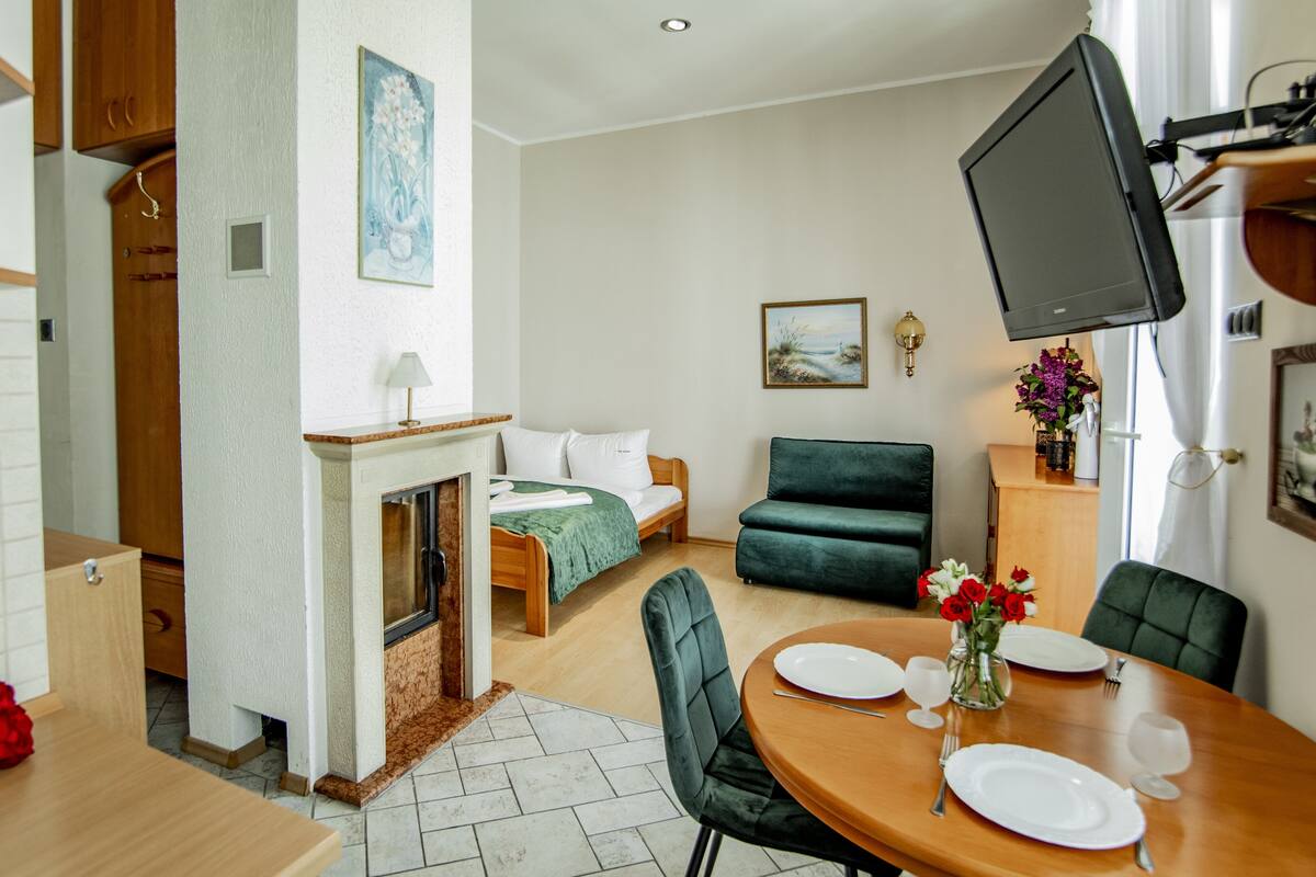 Een moderne woonkamer met een open haard, een eettafel gedekt voor twee personen, een groene bank en een flatscreen televisie aan de muur.
