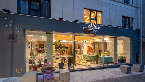 A hotel with a modern design, featuring a large glass facade, outdoor seating area, and a visible interior with a sofa and plants. - Athens Starlight Hotel (Athens)