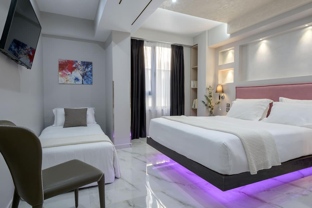 A hotel room with two beds, a TV mounted on the wall, a chair, and a painting.