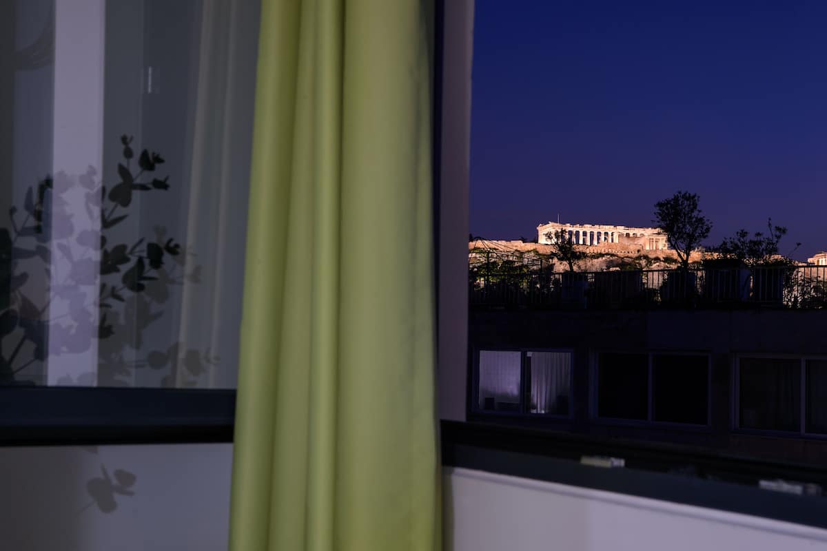 A view of the Parthenon illuminated at night from a window with curtains.