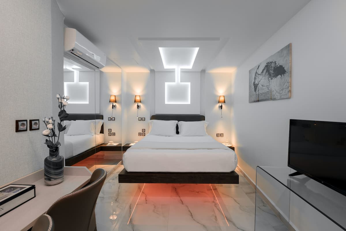 A modern hotel room with a bed, bedside lamps, a flat-screen TV, a desk with a vase of flowers, and a painting on the wall.