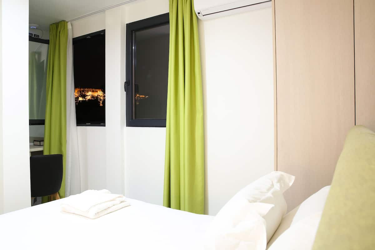 A hotel room with a bed, a window with curtains, a desk, and a chair.