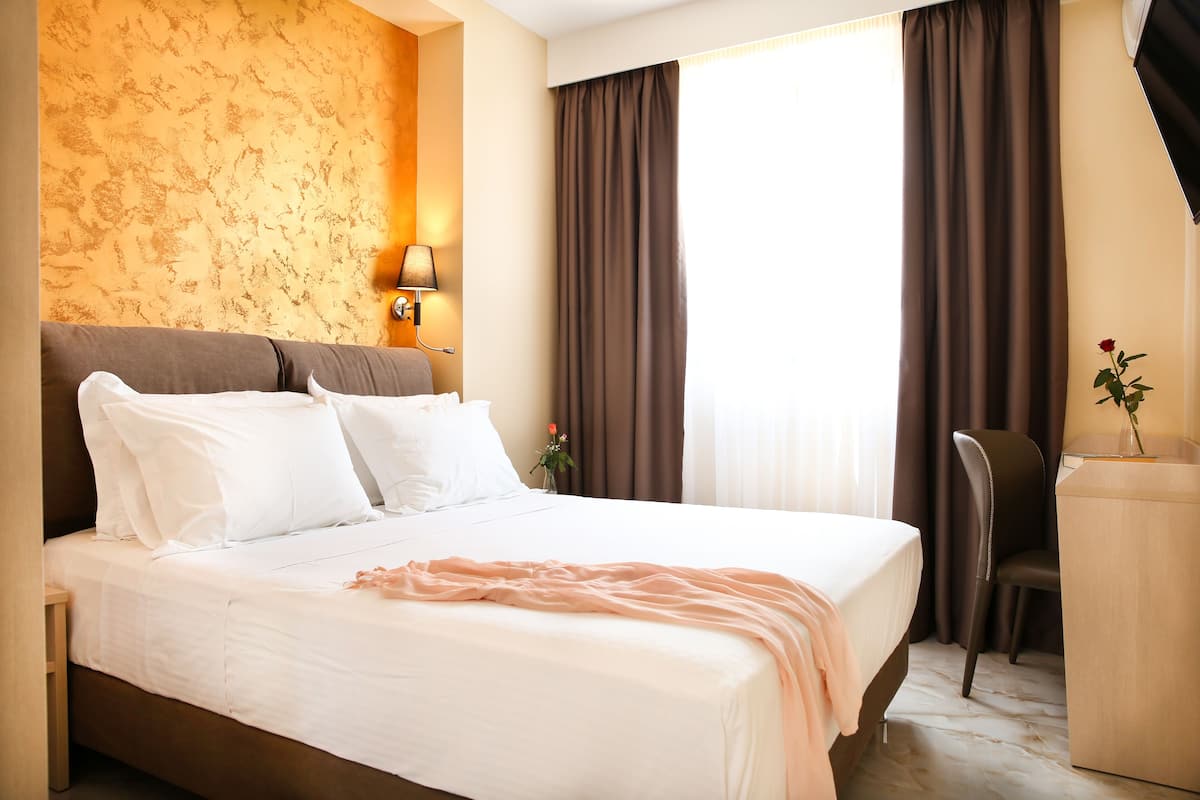 A hotel room with a large bed, a desk, and a chair.