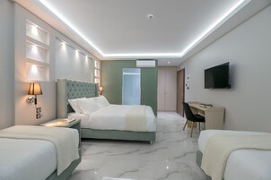 A hotel room with a bed, two bedside tables, a desk, a chair, a TV, and an air conditioning unit.