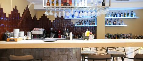 A bar area with a counter, shelves of liquor bottles, hanging glasses, and bar stools.