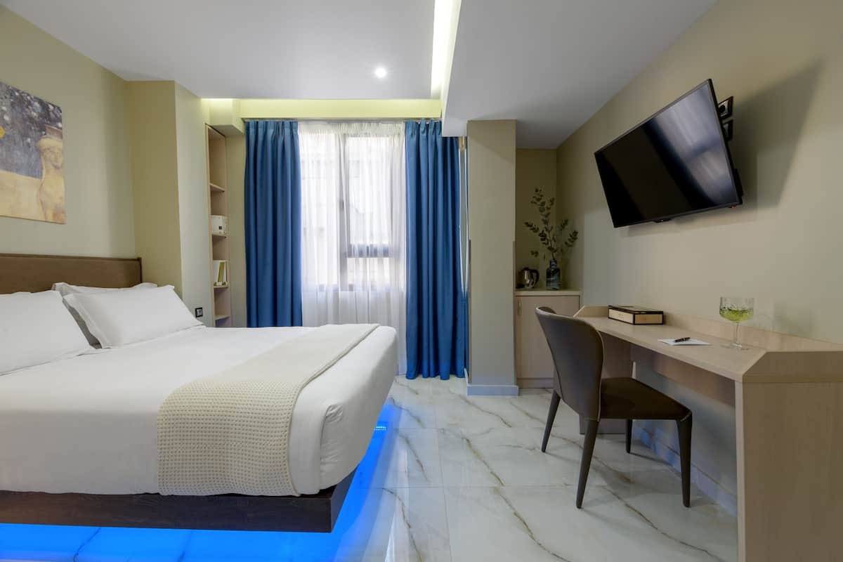 A hotel room with a bed, a desk, a chair, a TV, and a window with curtains.