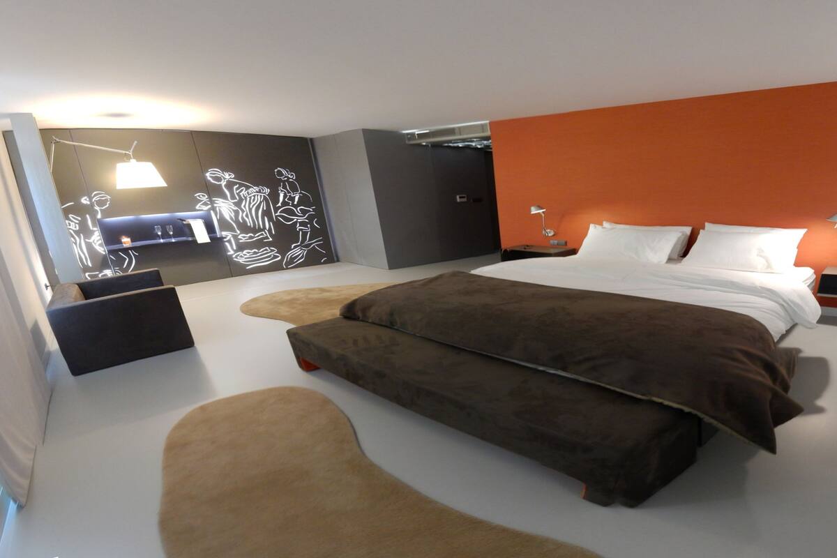 A modern bedroom with a large bed, a bedside table, a nightstand, and a wall-mounted lamp.
