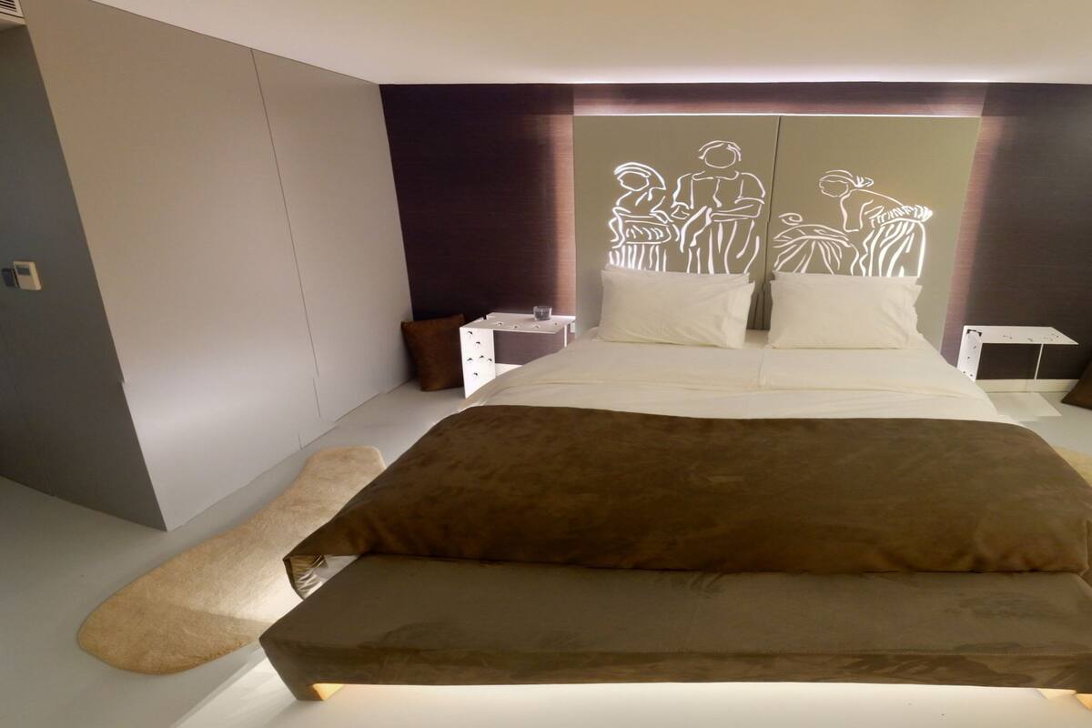 A modern bedroom with a large bed, two bedside tables, and a unique wall art installation.