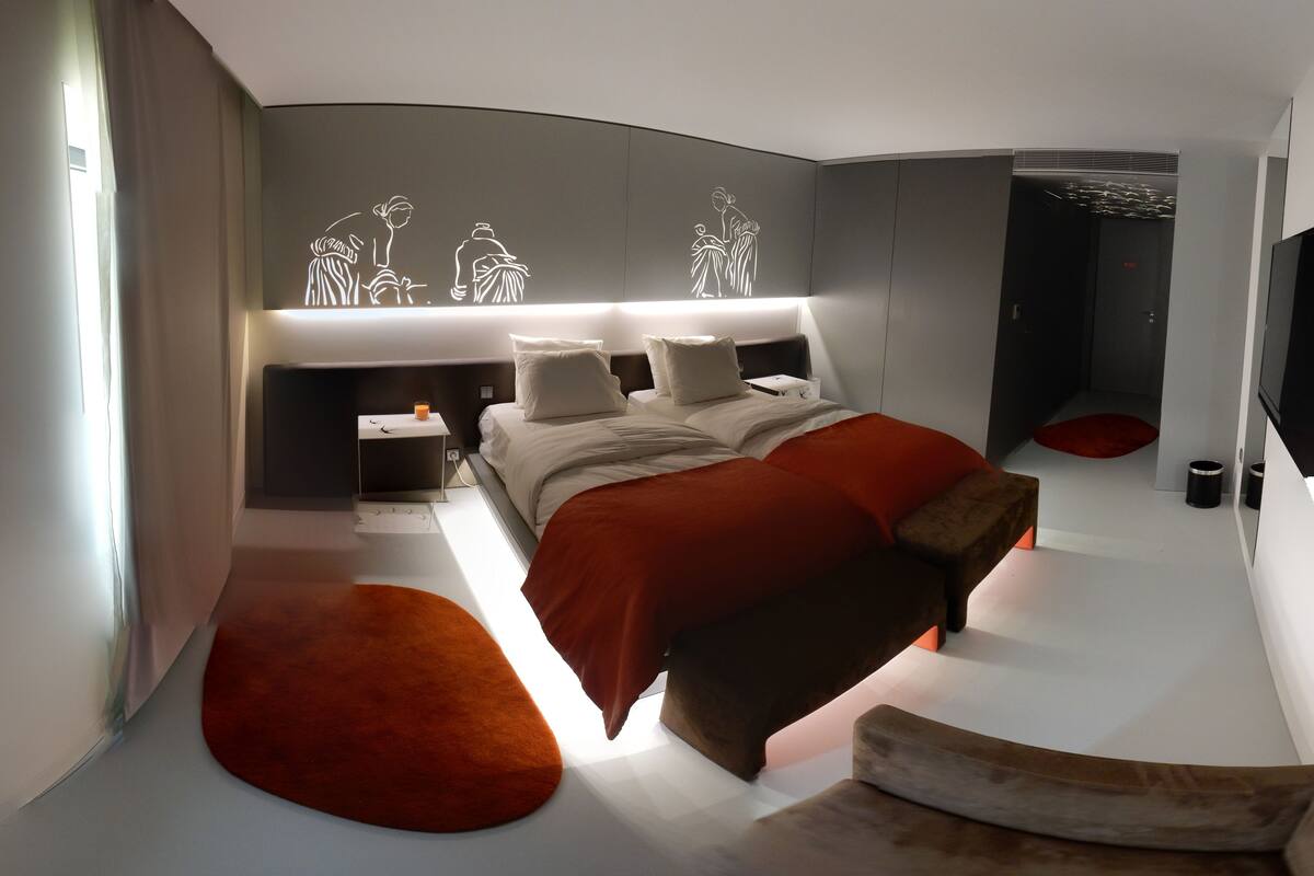 A modern bedroom with a curved bed, bedside tables, and a headboard with a lighted design.