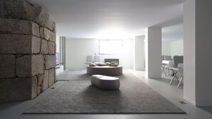 A modern living room with a stone wall, two round seating areas, a flat-screen TV, and a large window providing natural light. - Quinta das Lavandeiras - Caldas de Vizela (Vizela)