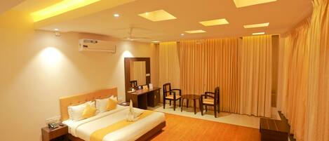 A hotel room with a large bed, bedside table, desk, chair, and curtains.