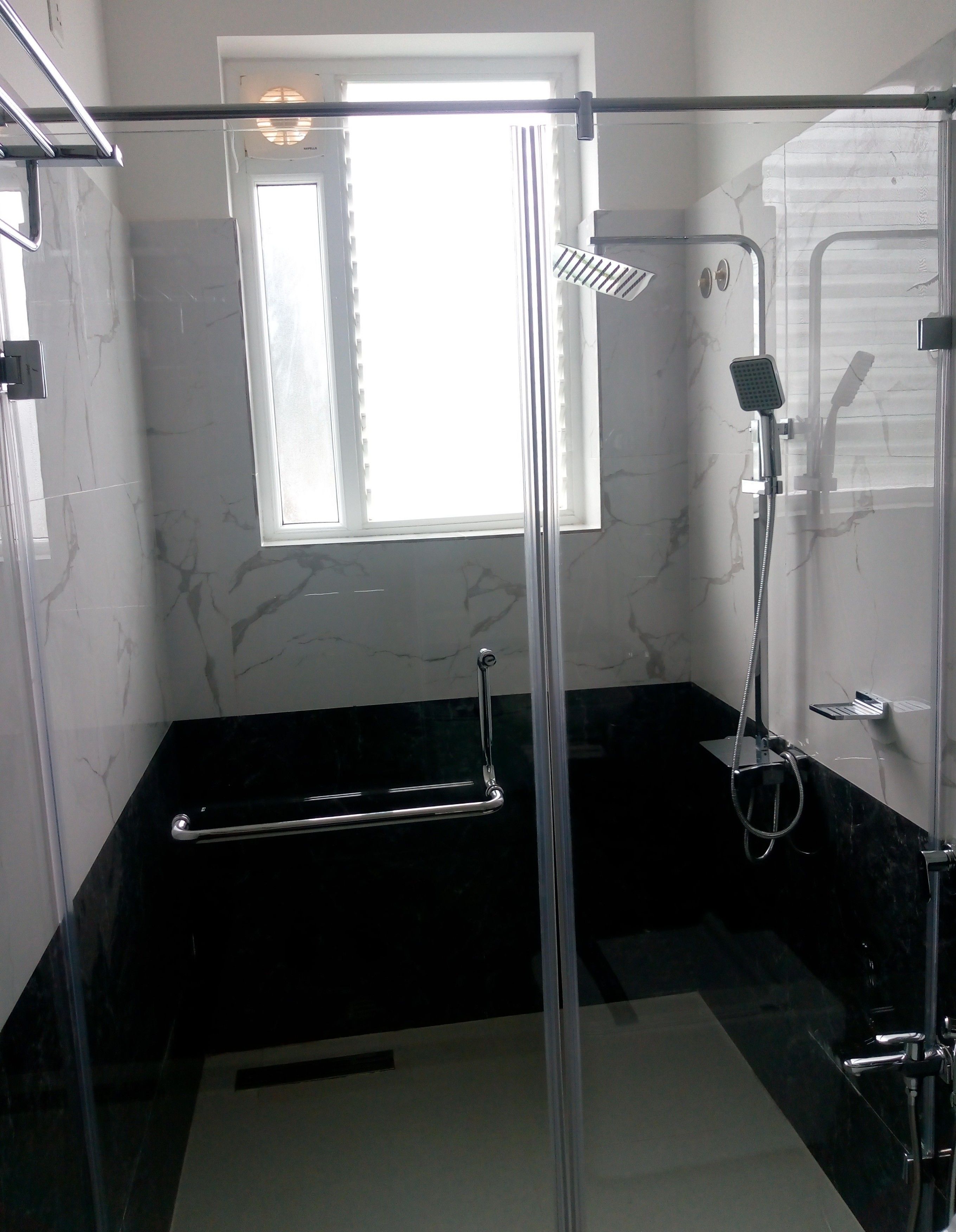 Ein modernes Badezimmer mit Duschkabine aus Glas, einer Handbrause, einem Handtuchhalter und einem Fenster für natürliches Licht.