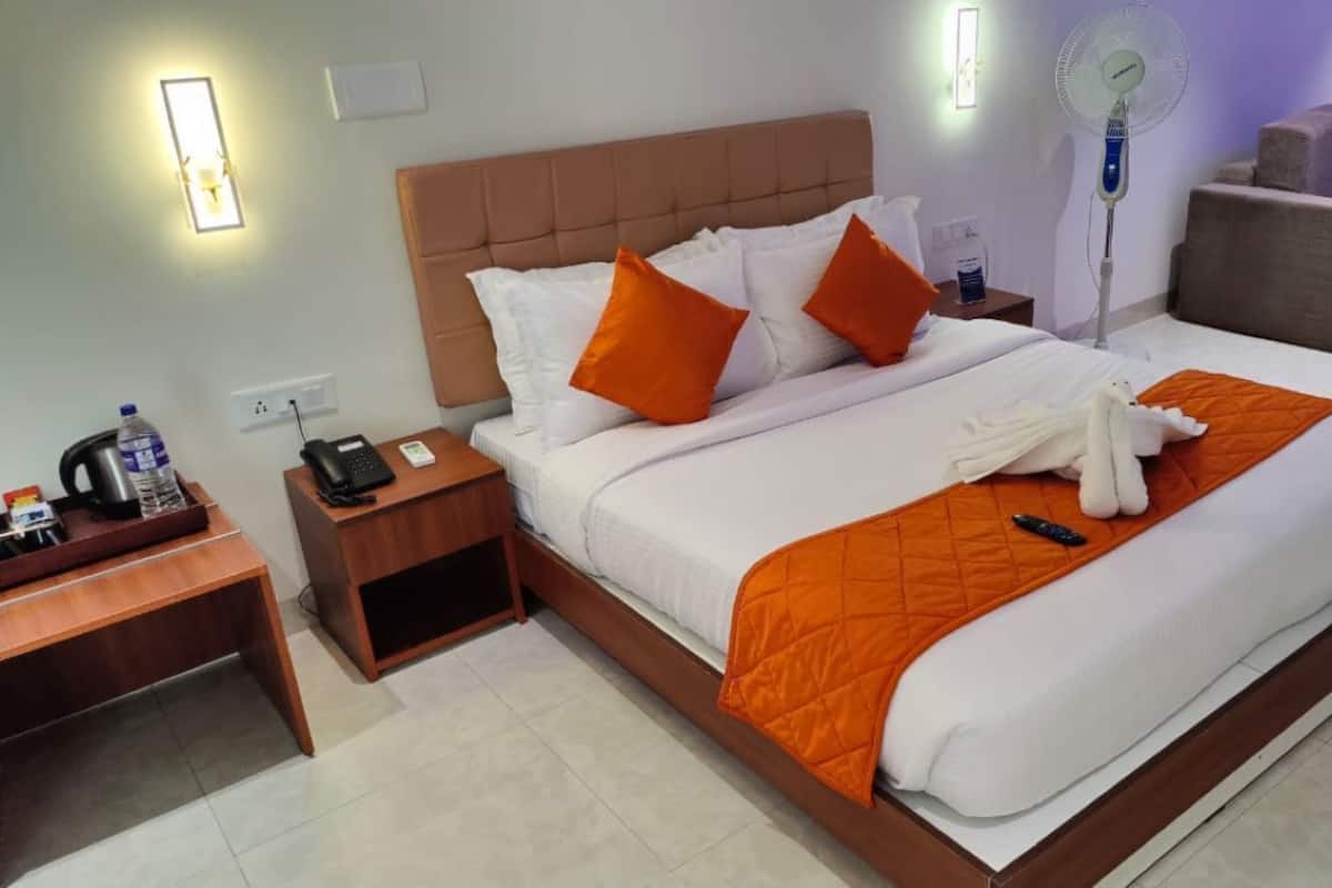 Habitación de hotel con una cama, una mesita de noche con un teléfono y una botella de agua, un ventilador y un sofá al fondo.