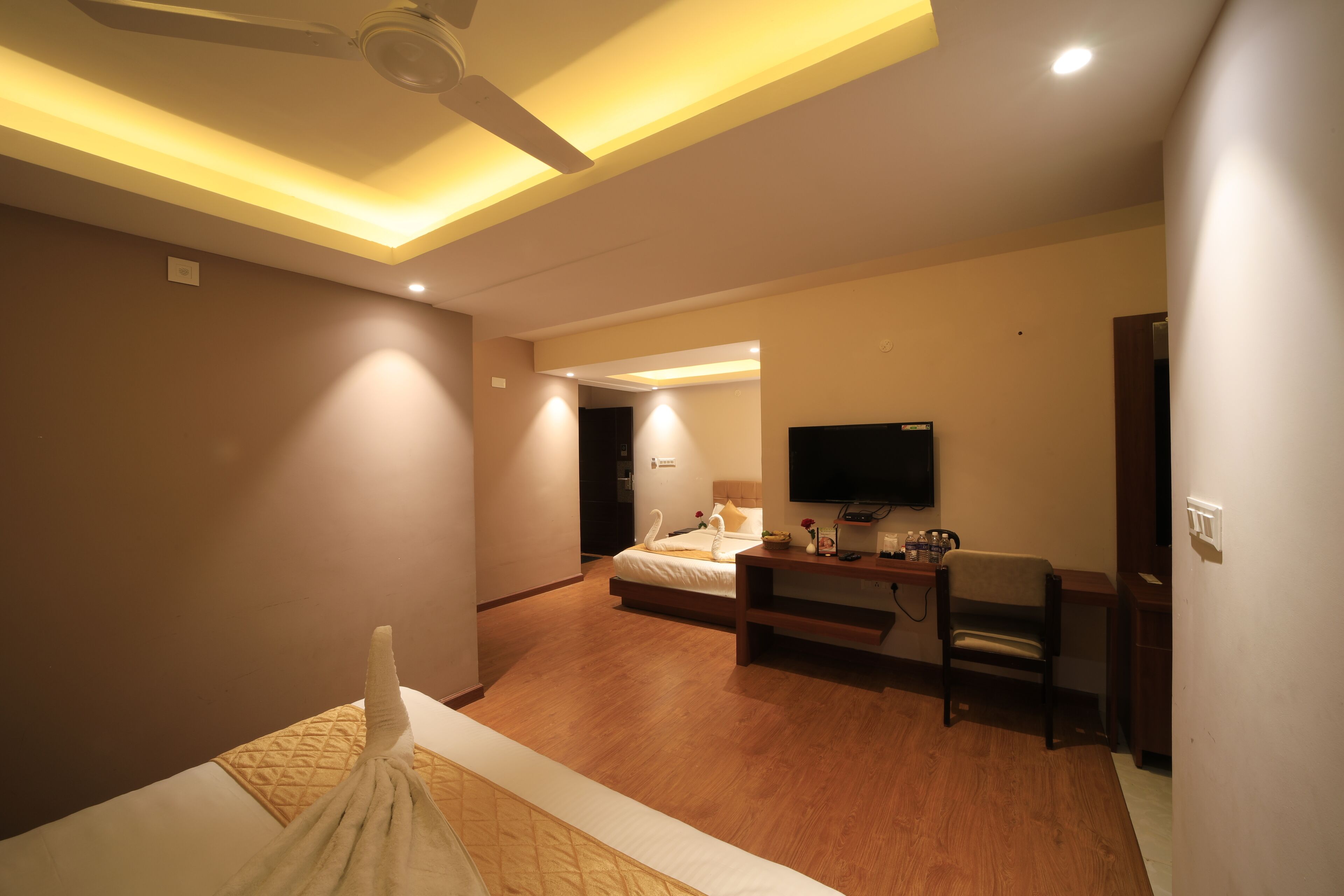 A hotel room with a bed, a desk, a chair, a flat-screen TV, and a ceiling fan.