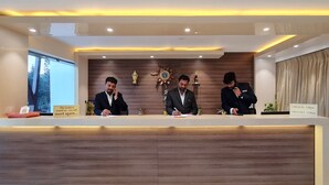 Een receptiebalie met drie medewerkers, houten lambrisering, trofeeën en een klok aan de muur.