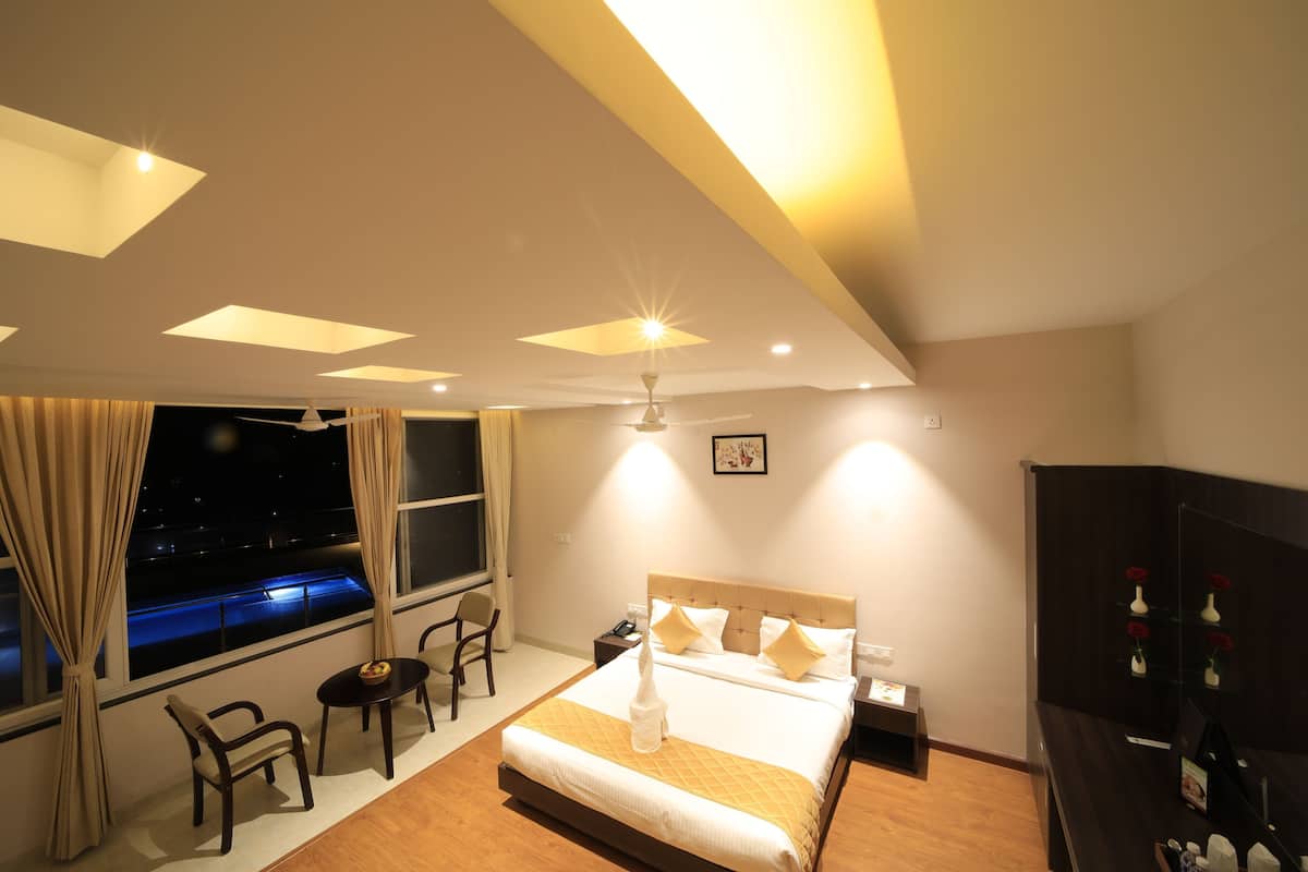 Habitación de hotel con cama, escritorio, silla, mesita de noche y una ventana grande con cortinas.