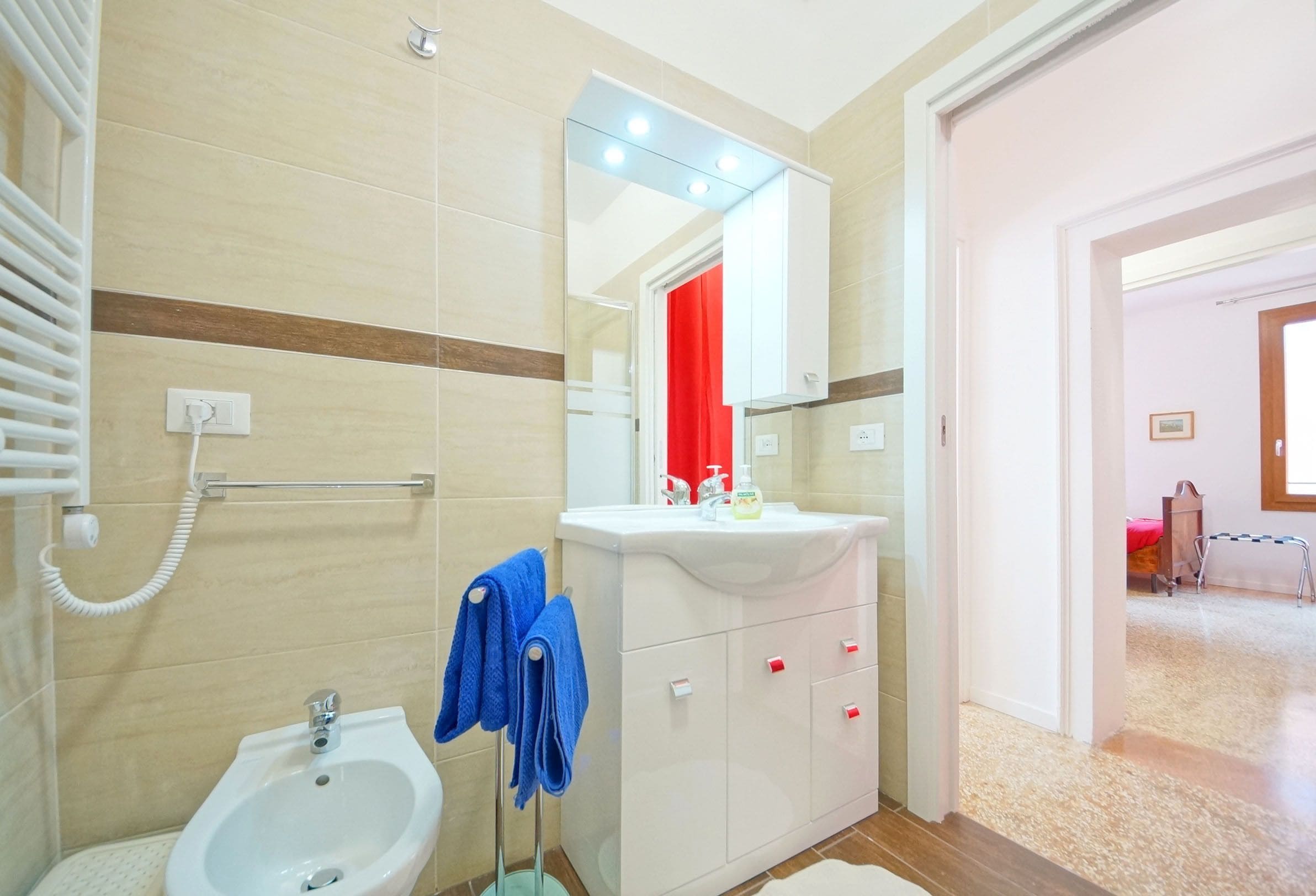 Une salle de bain équipée d’un bidet, d’un lavabo avec un miroir au-dessus et d’un porte-serviettes avec des serviettes bleues.