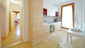 A modern kitchen with wooden cabinets, a built-in oven, and a dining area with a table and chairs. - DolceVita Apartments N. 372 (Venice)