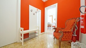 A room with a bright orange wall, a wooden chair with a patterned cushion, a white bench, and a fire extinguisher mounted on the wall. - DolceVita Apartments N. 372 (Venice)