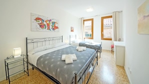 A bedroom with two beds, a glass bedside table, a wall art piece, and a window with curtains. - DolceVita Apartments N. 372 (Venice)