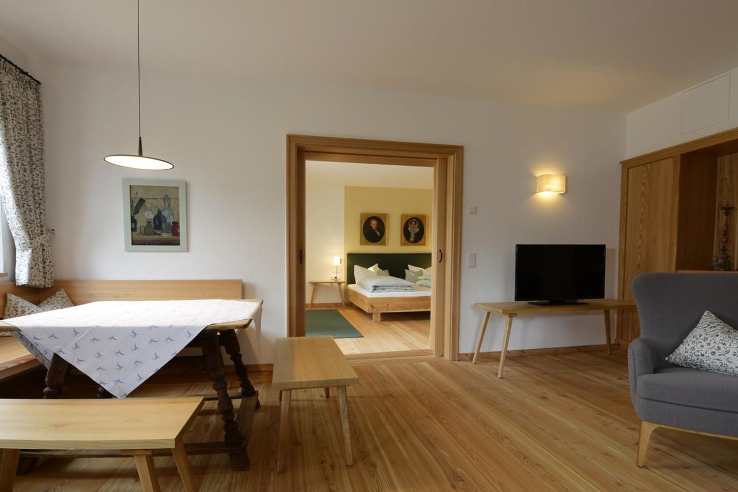 Ein gemütliches Zimmer mit einem Holzesstisch, einer Couch, einem Fernseher und einem Bett mit einem grünen Teppich.