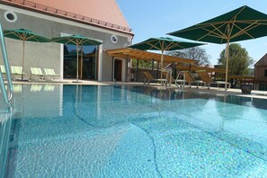 A swimming pool with lounge chairs and umbrellas, a building with a tiled roof, and a clear sky. - Romantik Hotel Zum Klosterbräu (Neuburg)