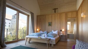 A bedroom with a large bed, wooden walls, a balcony, and a view of buildings outside. - Romantik Hotel Zum Klosterbräu (Neuburg)