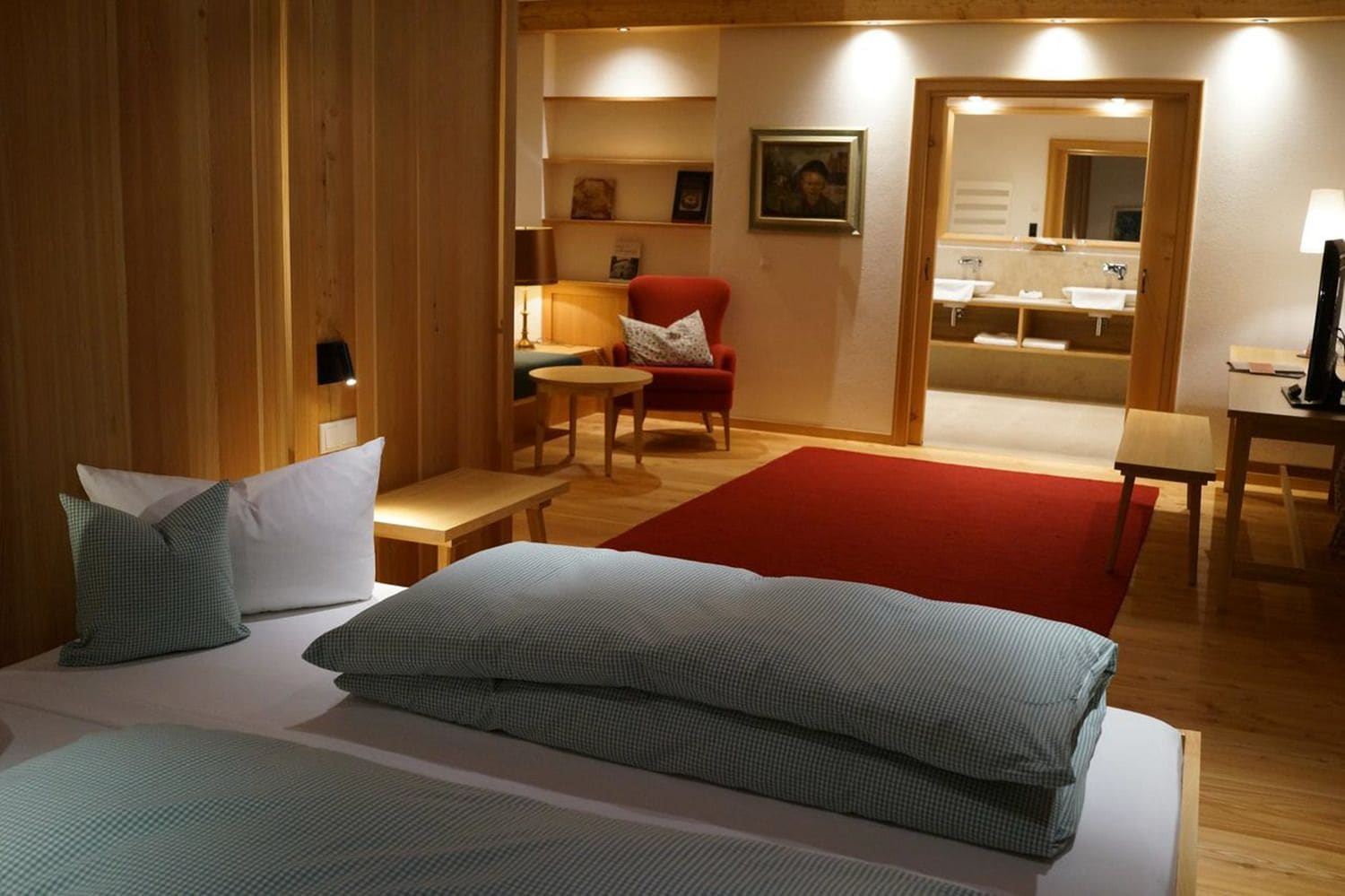 Ein Hotelzimmer mit einem Bett, einem kleinen Tisch, einem Stuhl, einem roten Schlafsofa und einem durch eine offene Tür einsehbaren Badezimmer.