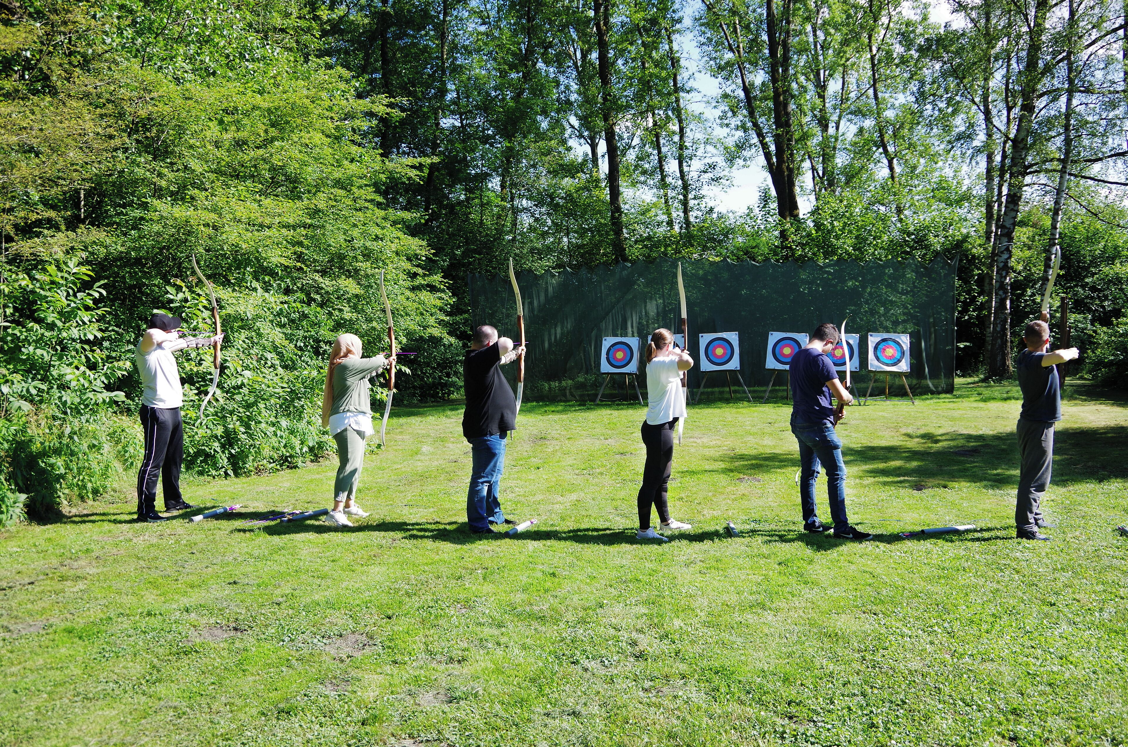 Eine Gruppe von Menschen übt im Freien Bogenschießen mit Zielscheiben.