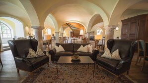 A spacious living room with a large brown leather sofa set, a patterned rug, and a high arched ceiling. - Romantik Hotel Zum Klosterbräu (Neuburg)