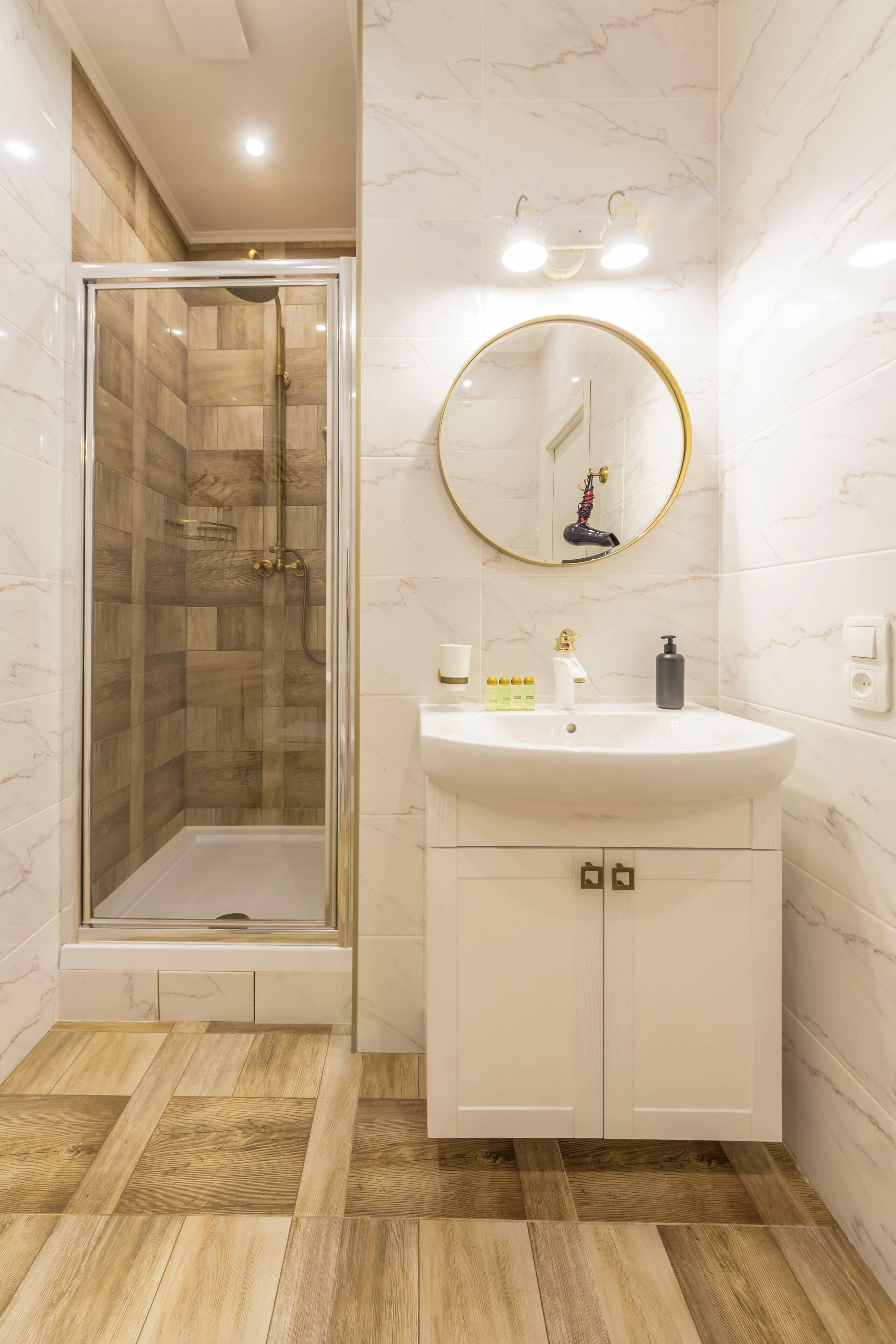 A modern bathroom with a glass-enclosed shower, a white vanity with a gold faucet, and a marble-tiled wall.