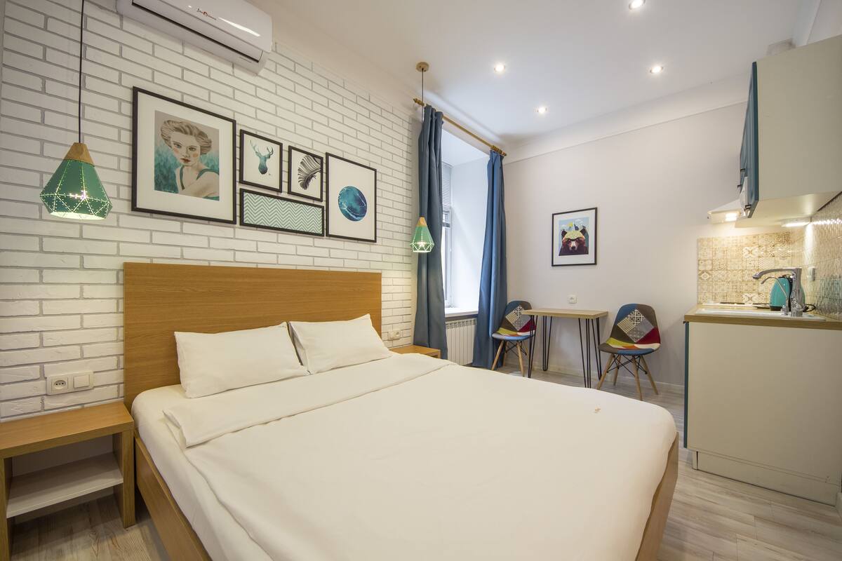 A hotel room with a large bed, a wooden headboard, a small table, a chair, and a kitchenette.