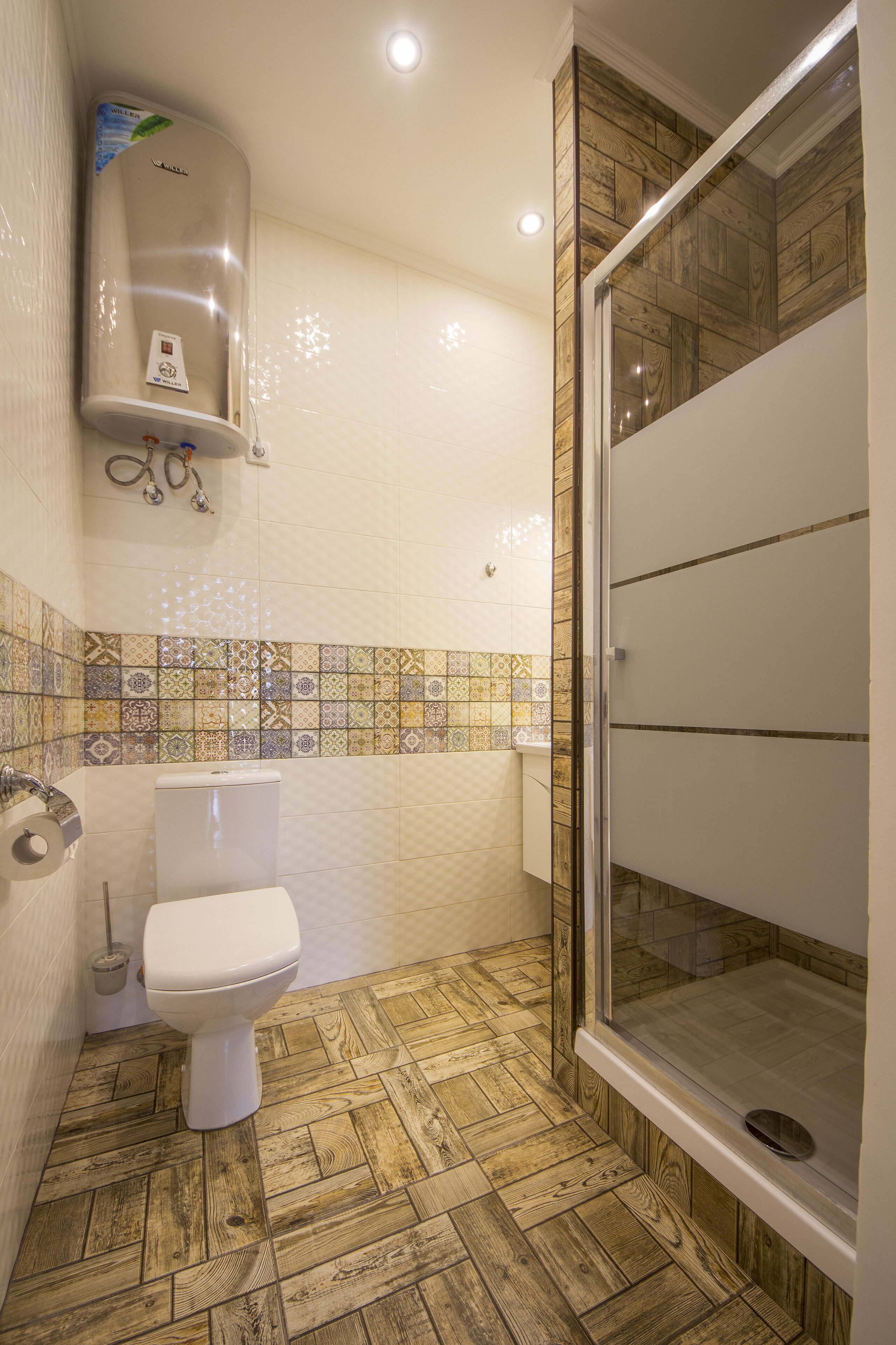 A bathroom with a toilet, a shower, and a tiled wall.