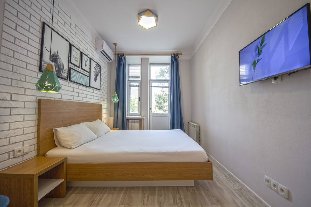 A bedroom with a wooden bed, a TV on the wall, and framed pictures on the brick wall.