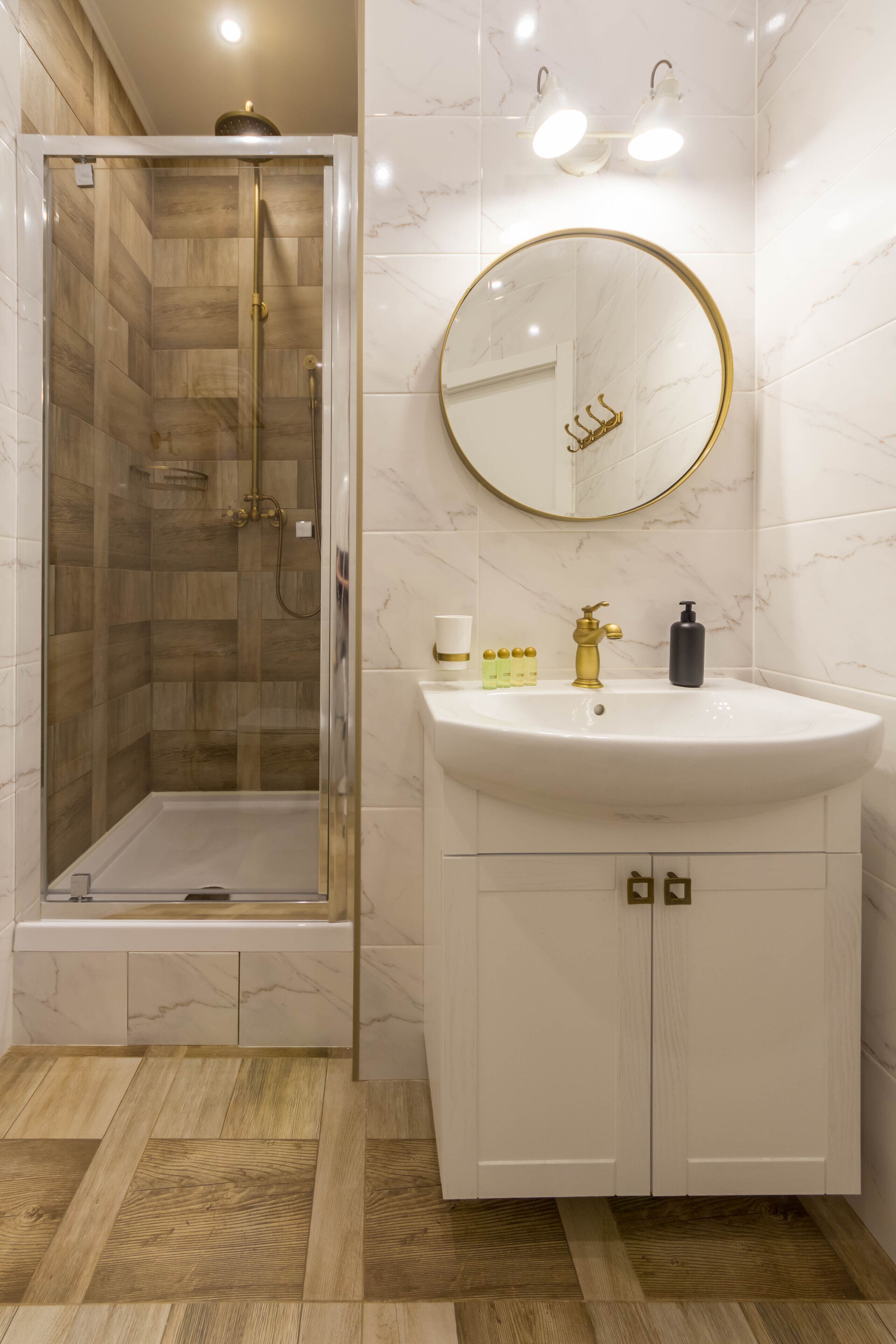 A bathroom with a glass-enclosed shower, a white sink with gold fixtures, and a marble-tiled wall.