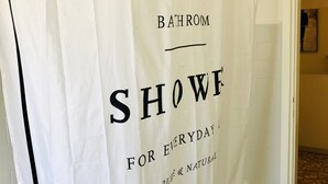 Une salle de bain avec un rideau de douche sur lequel est inscrit : « DOUCHE POUR UNE HYGIÈNE QUOTIDIENNE, NATURELLE ET SAINE ».