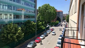 Une vue de rue avec des voitures garées, un cycliste et des bâtiments, dont une structure moderne en verre.