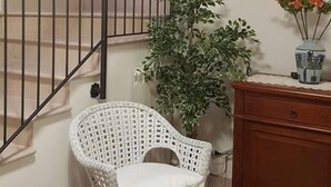 A staircase with a metal railing, a wicker chair, a potted plant, and a wooden cabinet. - Agata (Cocullo)