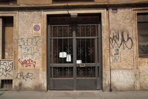 Une façade d’immeuble avec une entrée grillagée, des graffitis et un panneau indiquant qu’il est interdit de se garer.