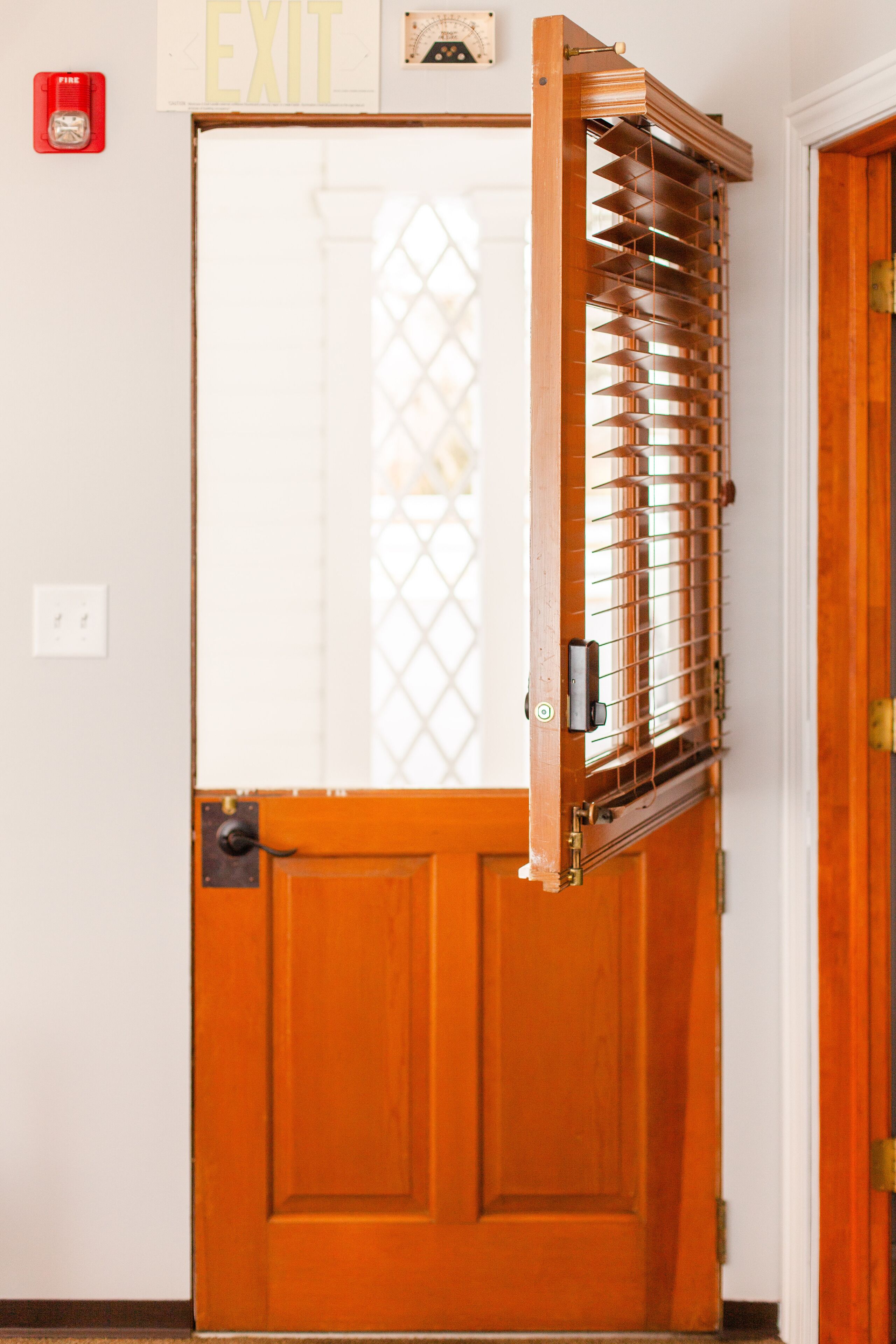 Une porte en bois avec une grille métallique à la fenêtre et un détecteur d’incendie fixé au mur.