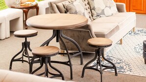 Ein Wohnzimmer mit einer Couch, zwei runden Tischen und einem Couchtisch. Im Hintergrund ist eine Holztür und ein Küchenbereich zu sehen.