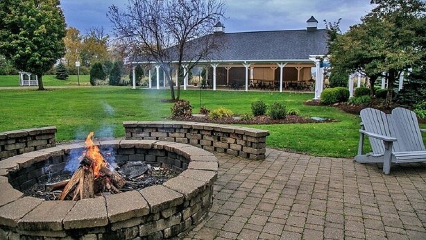 Ein Feuerkorb mit Backsteinkreis, eine überdachte Terrasse und ein Adirondack-Stuhl.