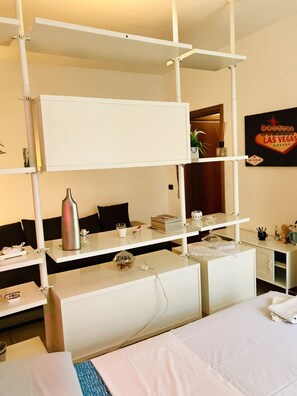 Quarto de hotel com cama beliche, uma escrivaninha com computador, uma pequena mesa com uma planta e um letreiro na parede com a inscrição 'Welcome to Las Vegas'.