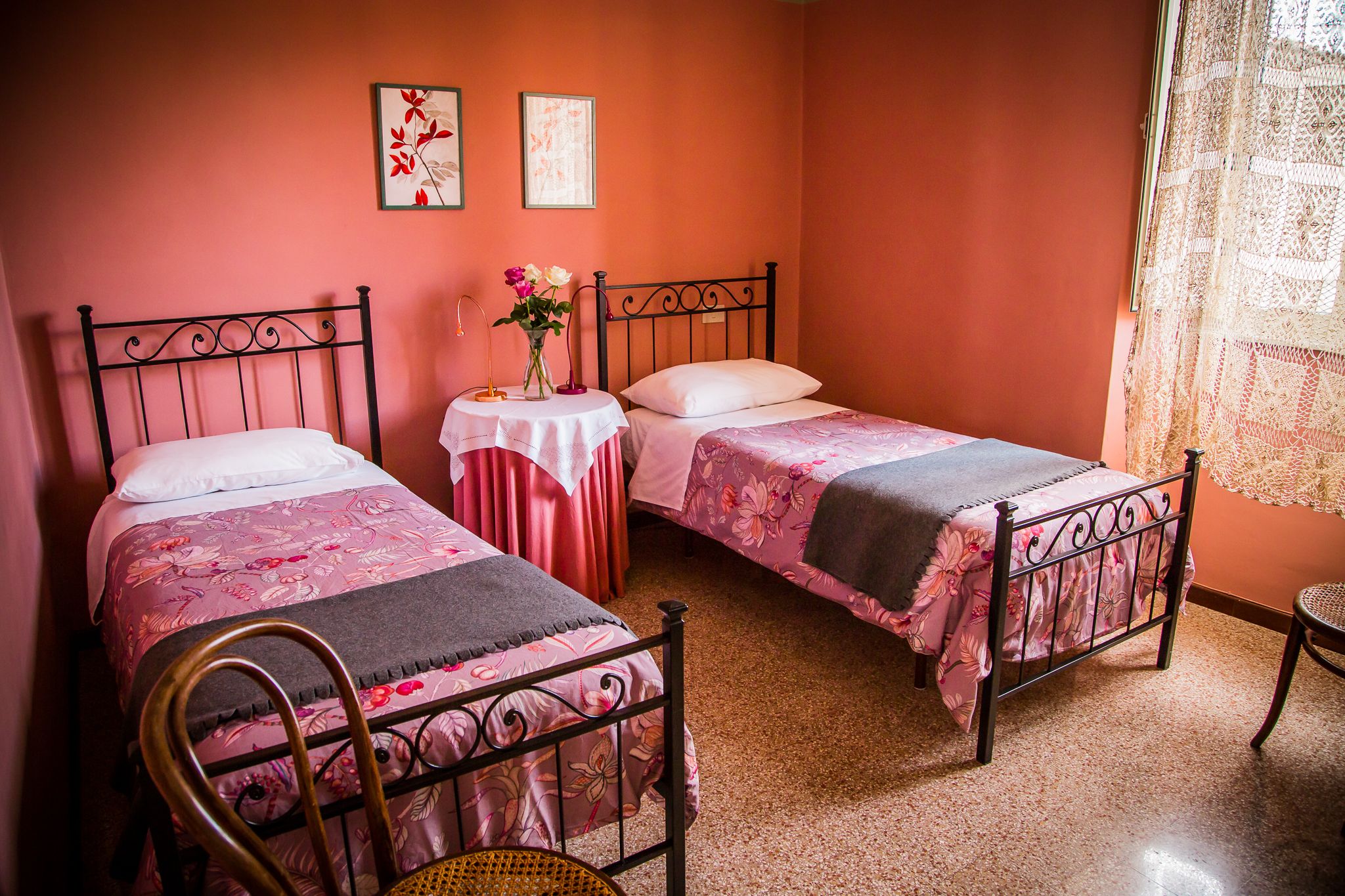 Une chambre avec deux lits simples, une petite table ronde ornée d’un vase de fleurs et une chaise.