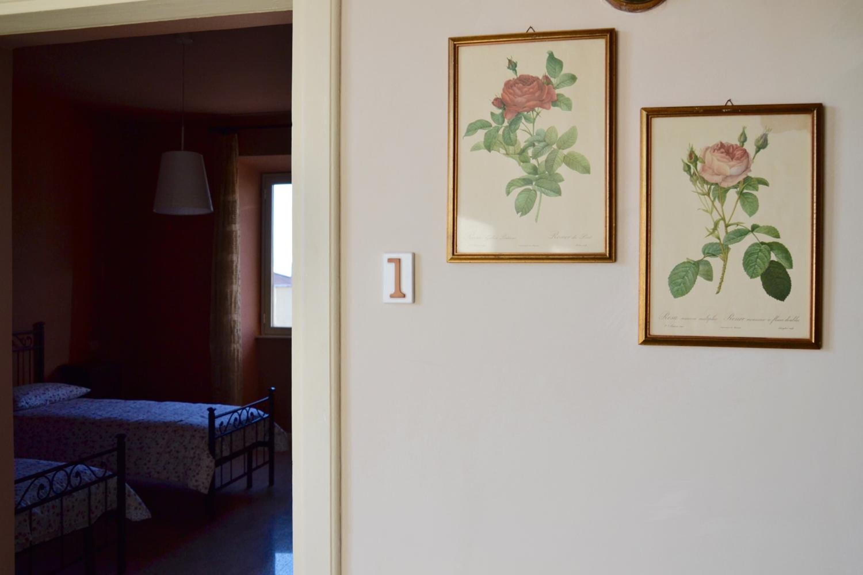 Habitació amb dos llits, un lluminària penjant i dues il·lustracions botàniques emmarcades a la paret.