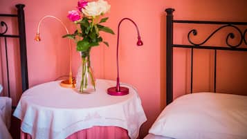 Una cama con un almohadón blanco, una mesa redonda con mantel blanco y un florero con flores.